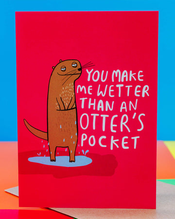 Bright pink greeting card by Rebel Romance featuring a quirky illustrated otter with water dripping off it, standing in a puddle. Bold white text reads "You make me wetter than an otter’s pocket." Designed by Katie Abey, this cheeky A6 card adds a fun and flirty touch to any gift. Ideal for Valentine’s Day, anniversaries, or playful notes. UK indie brand Rebel Romance specialises in alternative cards, gifts, and retro-inspired designs.