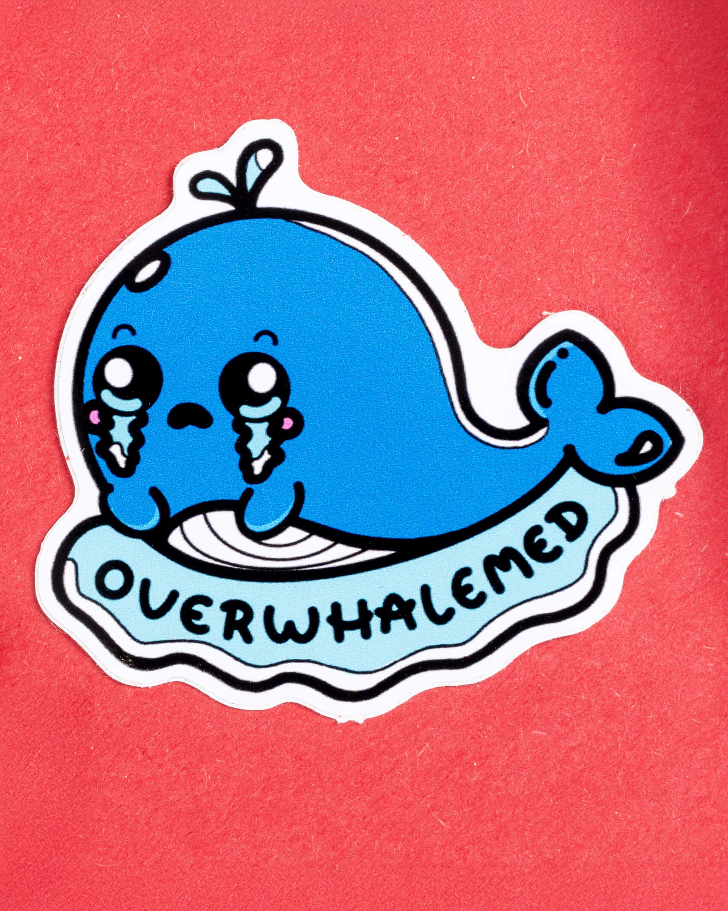 Cute blue vinyl whale sticker from Rebel Romance, featuring a crying cartoon whale with the word “OVERWHALEMED” in bold text below. Designed by Innabox, this waterproof 5x5cm gloss vinyl sticker is whale-shaped and perfect for expressing emotional overload. Ideal for decorating laptops, notebooks, or water bottles. A fun mental health-themed gift from a UK indie brand embracing quirky, alternative style.