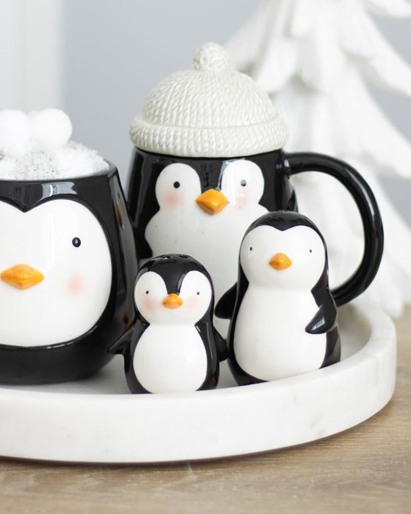 Two ceramic penguin salt and pepper shakers styled with matching penguin mugs on a white marble tray, creating a cosy winter kitchen display.