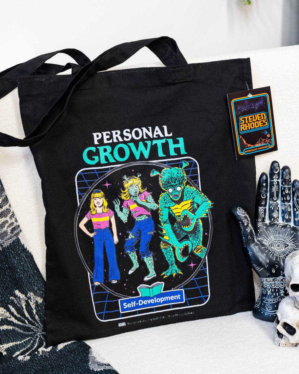 A black tote bag featuring Steven Rhodes’ “Personal Growth” design, showcasing a retro-inspired self-development illustration with vibrant neon colours and a humorous theme. The tote includes long handles for easy carrying and is labelled as officially licensed merchandise. Perfect for shopping, work, or travel.