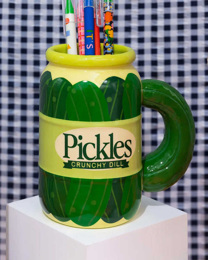 A ceramic pickle jar-shaped mug from Rebel Romance, styled as a quirky pen holder. Features the label "Pickles Crunchy Dill" and a green pickle-shaped handle. Perfect for lovers of novelty kitchenware or unique desk decor.