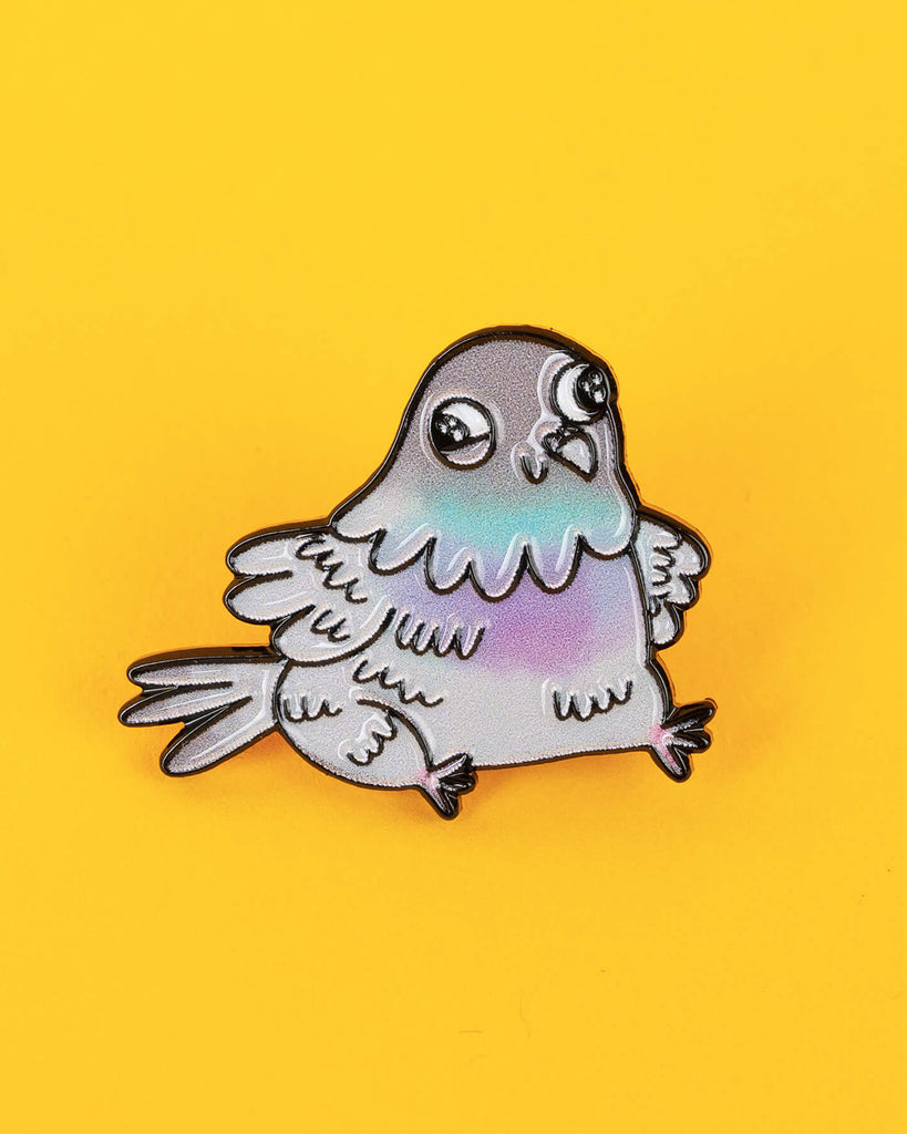 Another close-up of the pigeon pin showing the rounded cartoon style and pastel colouring, laid flat on a yellow surface.