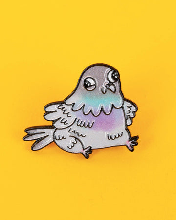 Another close-up of the pigeon pin showing the rounded cartoon style and pastel colouring, laid flat on a yellow surface.