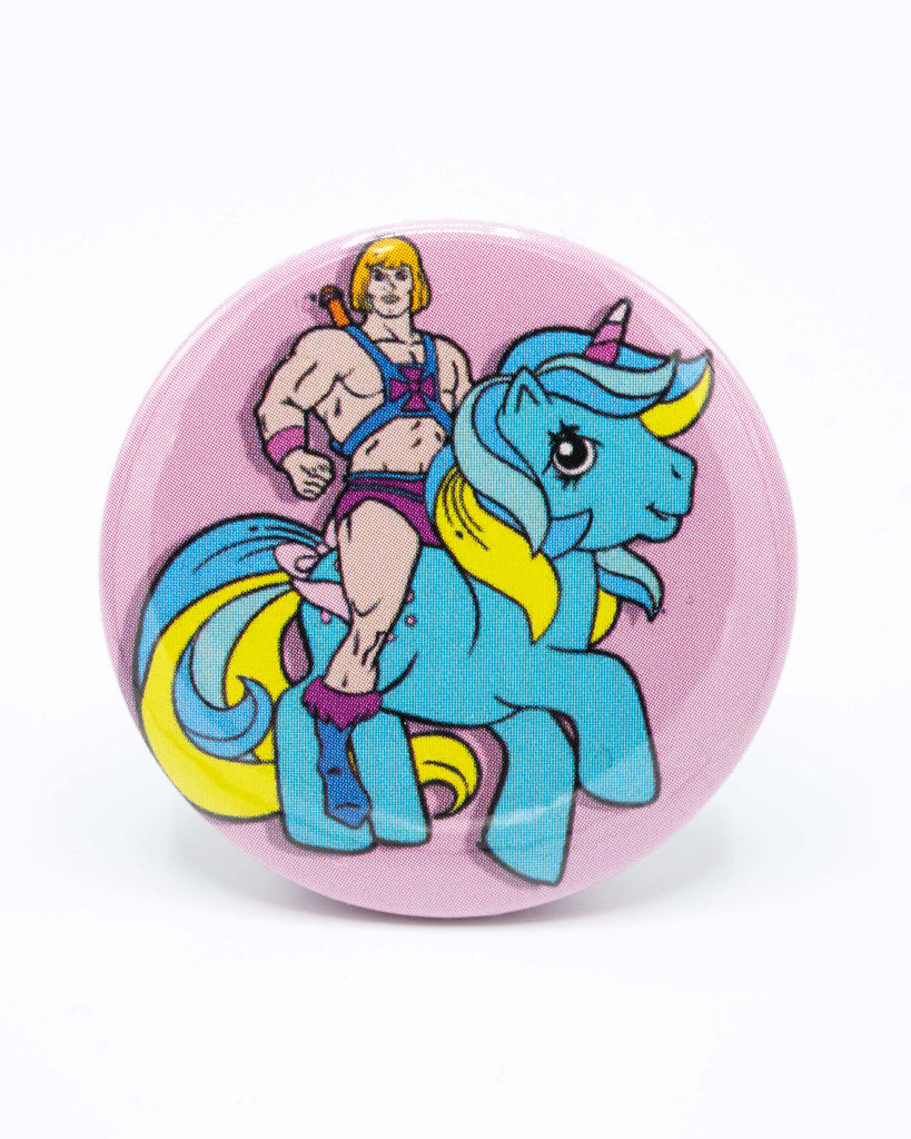 Pink button badge with a cartoon character, he man, riding a blue my little pony unicorn. A retro 80s design from Bite Your Granny.