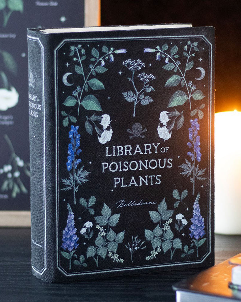 Aesthetic photo of the "Library of Poisonous Plants" book-shaped box on a dark table with candlelight in the background. A perfect gothic-style storage solution by Rebel Romance, a UK small business.