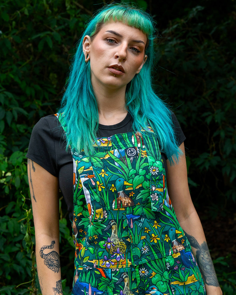 Claudia models the Rebel Romance Pond Birds Stretch Dungarees featuring a vibrant green wetland design with ducks, kingfishers, and pond flowers. Ethically made with comfy stretch cotton twill, these unisex dungarees celebrate slow fashion and inclusive sizing.