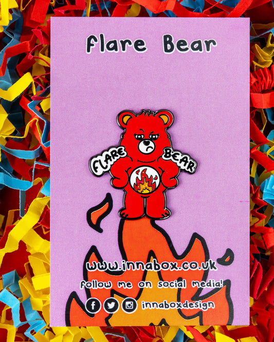 A cute glittery enamel pin badge featuring a red bear named Flare Bear on a lilac backing card with “Flare Bear” text. The design shows the bear with a glittery fire emblem on its belly, symbolising chronic illness flare days. Surrounded by red, yellow, and blue paper confetti. Sold by Rebel Romance, a UK brand for alternative fashion and gifts.