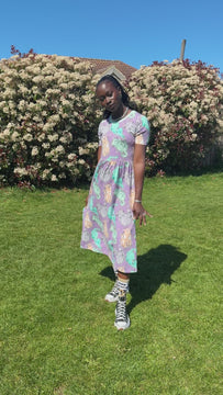 Video of Rebel Romance x Abi Perry Purrfect Cats Midi Stretch Dress with short sleeves and fitted waist. The lilac fabric features cute cat illustrations throughout. Styled with statement socks and trainers, ideal for fun, expressive alternative fashion lovers. Posing in a sunny green park in Hove.
