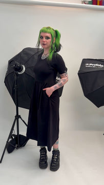 Alternative model in Rebel Romance black midi dress with short sleeves and soft stretch fabric, moving in a white photography studio background. The relaxed skirt and comfortable fit highlight ethical slow fashion for alternative style lovers in the UK.