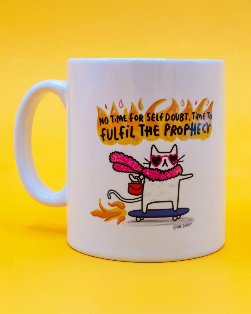 Straight-on view of Katie Abey’s Time To Fulfil The Prophecy Cat Mug on a yellow background. Showcases a sassy cat skating through fire with heart sunglasses and the iconic quote. Sold by Rebel Romance, an independent UK shop for alternative gifts and homeware.