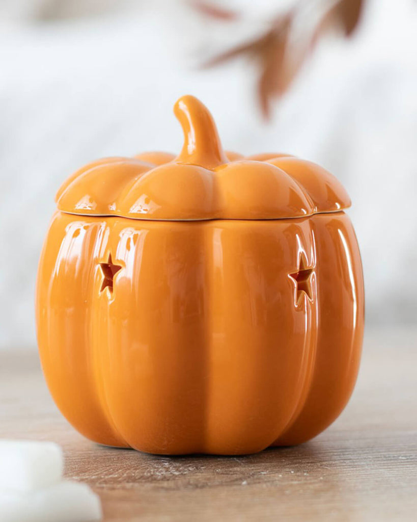 A close-up of the ceramic pumpkin oil burner with star-shaped cutouts, placed on a rustic wooden surface.
