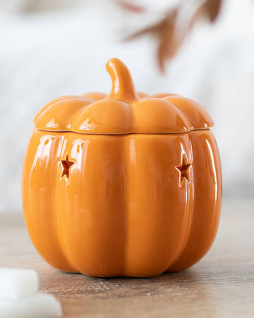 A close-up of the ceramic pumpkin oil burner with star-shaped cutouts, placed on a rustic wooden surface.