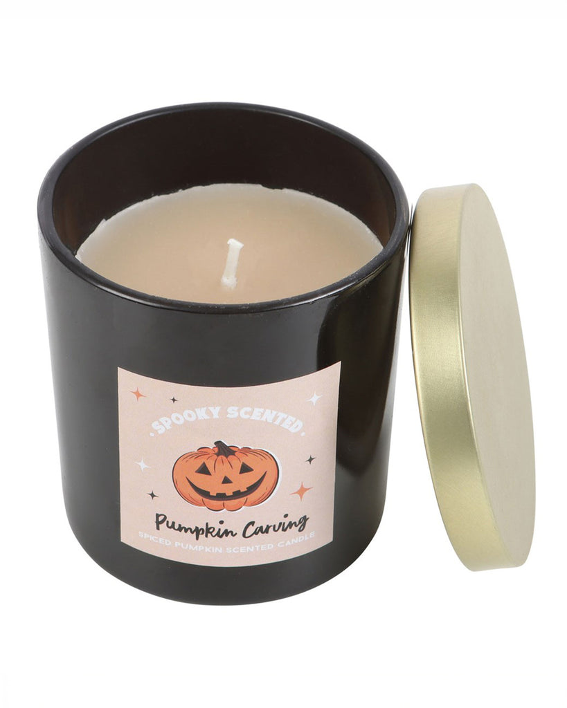 A black glass jar containing the Pumpkin Carving candle, with a gold metal lid and a spooky pumpkin-themed label.