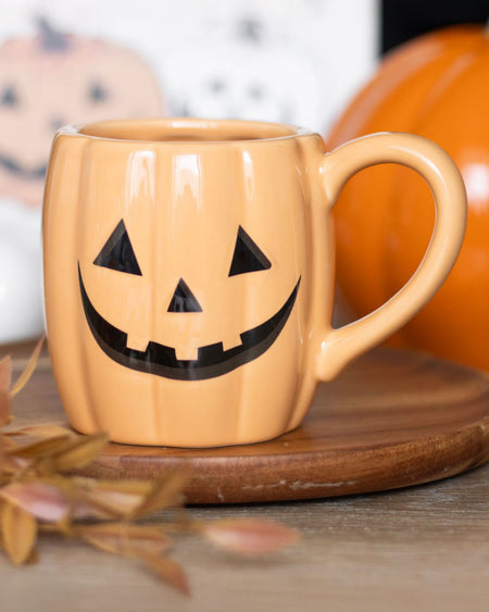 Close-up of the Jack-o'-Lantern ceramic mug on a wooden board with autumn leaves and pumpkin decor in the background, perfect for Halloween drinks.