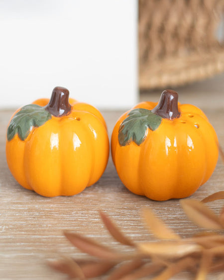 Lifestyle photo of Rebel Romance pumpkin salt and pepper shakers placed on a rustic wooden table. Their glossy orange finish and leafy detail stand out, adding seasonal charm to your autumn or Halloween dining setup.