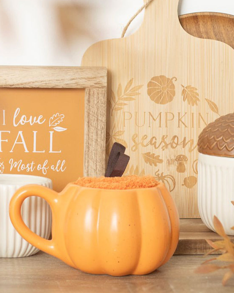Pumpkin-shaped orange ceramic mug with fluffy socks inside, styled on a wooden surface with autumn-themed signs reading “I love fall” and “Pumpkin season.” A cosy autumnal scene from Rebel Romance, a UK brand for alternative millennials.