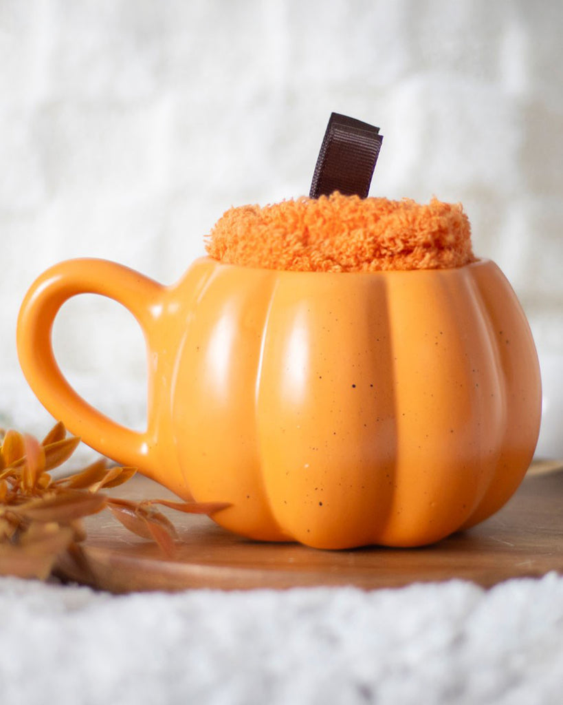 Close-up lifestyle shot of Rebel Romance’s pumpkin mug set on a rustic tray with faux foliage, filled with fluffy socks. A perfect autumn homeware piece.