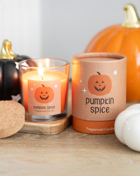 A close-up of the Peekaboo Pumpkin Spice scented candle in a glass jar with a cork lid, featuring a jack-o'-lantern label and a rich orange wax.