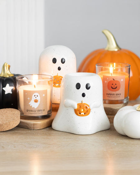  cosy Halloween scene featuring the Peekaboo Pumpkin Spice Candle from Rebel Romance, glowing warmly among autumn decorations, including ceramic ghosts, mini pumpkins, and other seasonal candles.