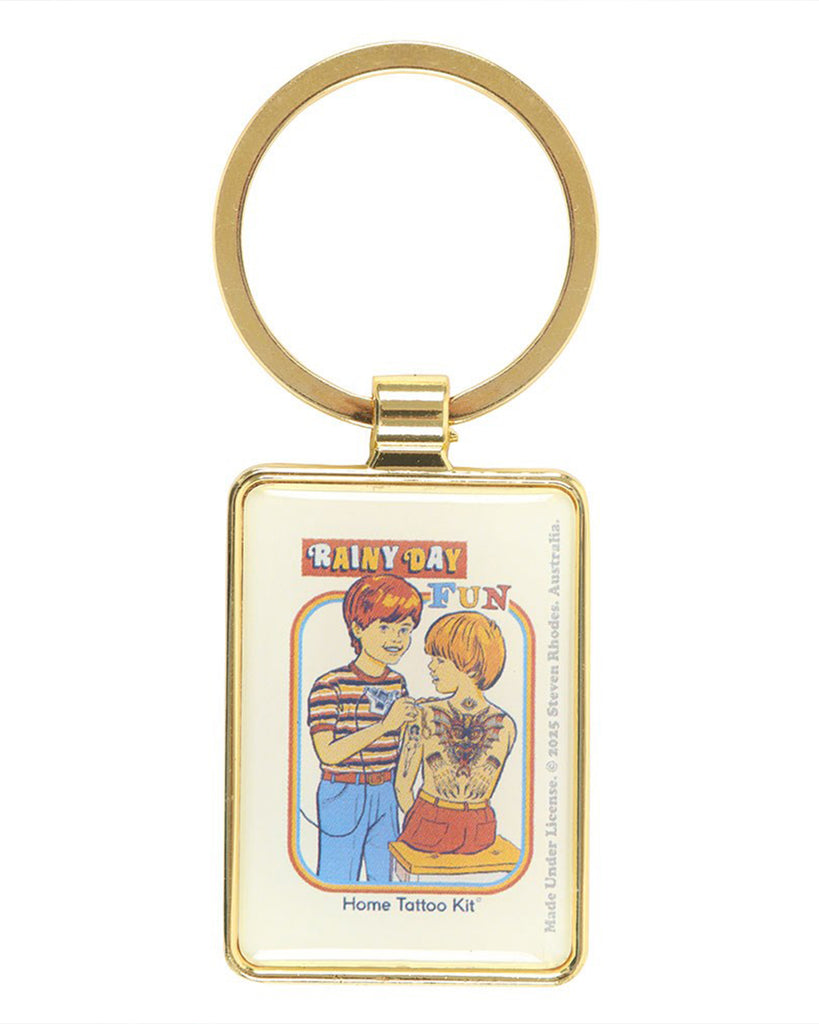 Front view of the Steven Rhodes Rainy Day Fun Keyring from Rebel Romance. The enamel keyring has a shiny gold finish and features vintage-inspired tattoo artwork with the text “Home Tattoo Kit.” A quirky, alternative gift for millennials who love retro humour and unique accessories.