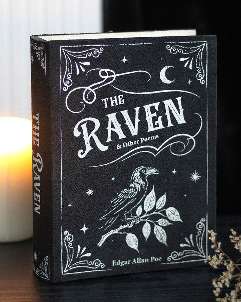 A styled photo of The Raven book-shaped box on a dark table with a candle glowing in the background, enhancing its mysterious, gothic charm. This secret storage piece is sold by Rebel Romance, a UK alternative lifestyle brand.