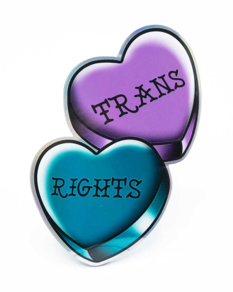A holographic vinyl sticker of two overlapping heart shapes – one purple, one teal – with the words “TRANS RIGHTS” written across them in bold black lettering. A bright and empowering LGBTQ+ design.