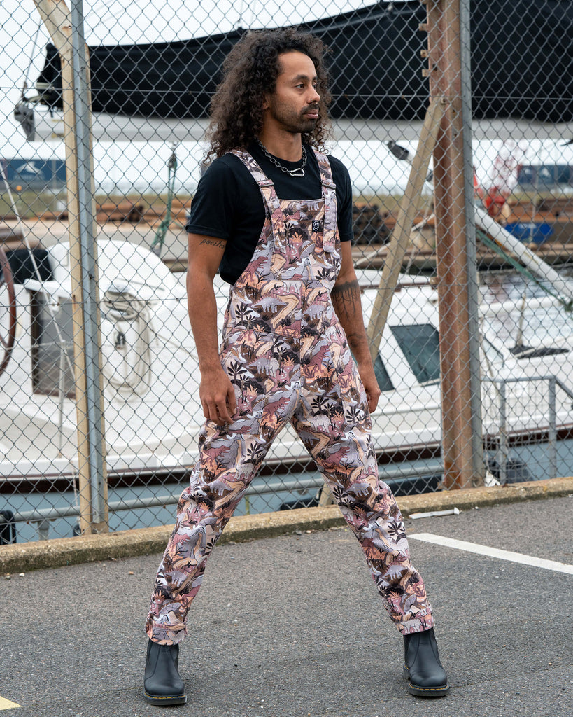 Richard standing with legs apart in Rebel Romance Dinoverse Dungarees, showing relaxed fit and vibrant all-over dinosaur design.