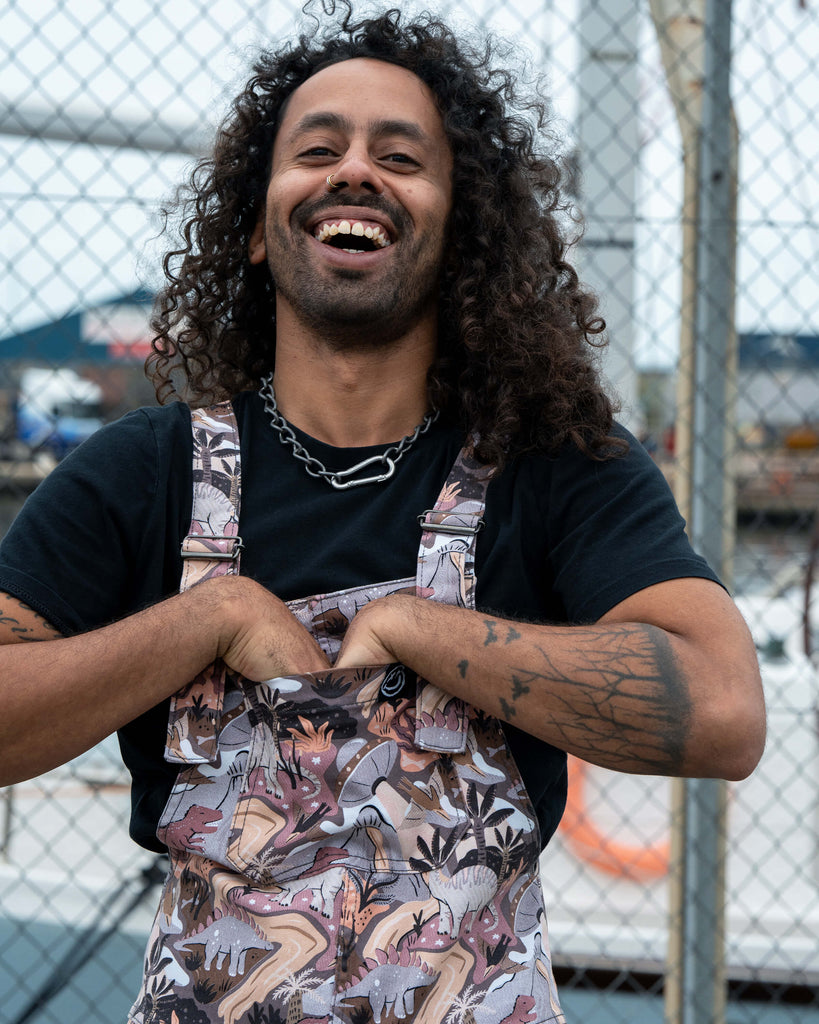 Richard laughing with hands tucked into the front bib pocket while wearing Rebel Romance Dinoverse Dungarees, showing the fun and quirky style.
