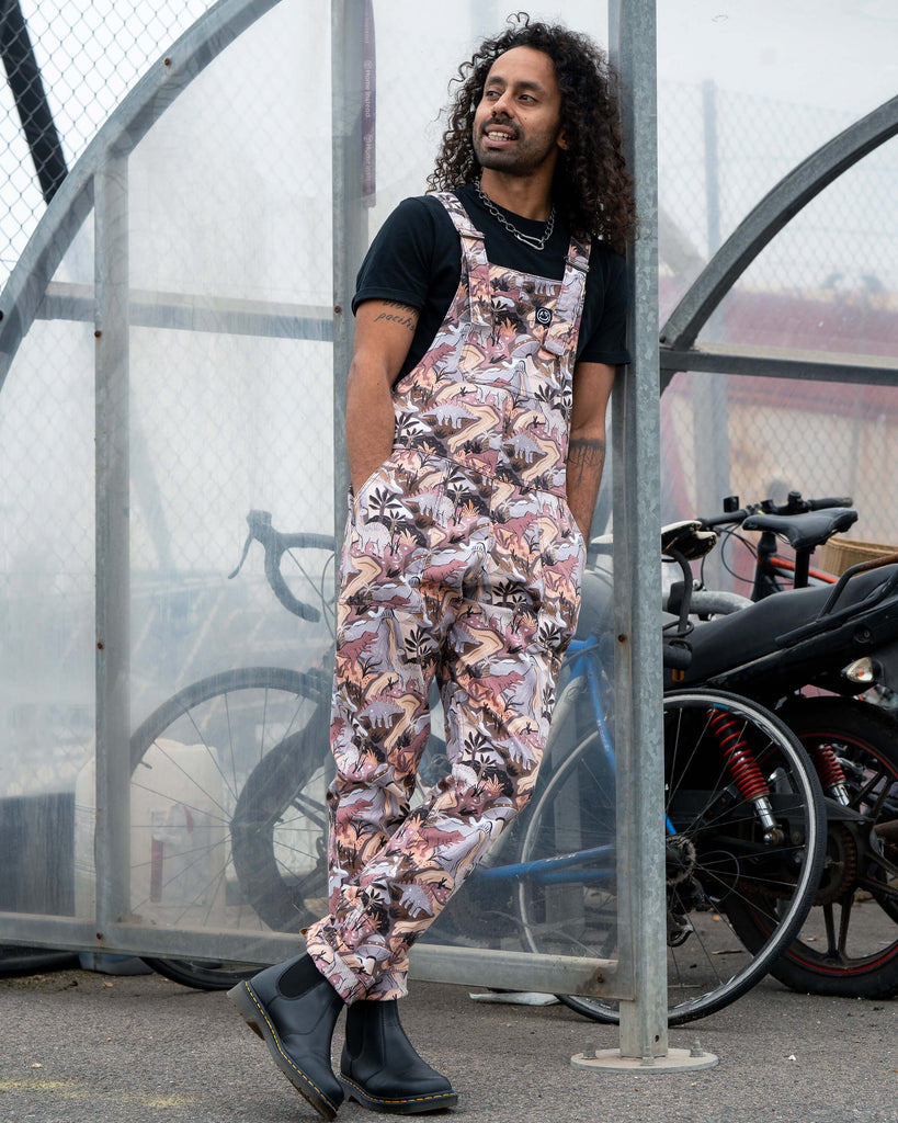 Richard wearing Rebel Romance Dinoverse Stretch Twill Dungarees with hands in pockets, leaning casually by a bike rack, showing the playful dinosaur print.