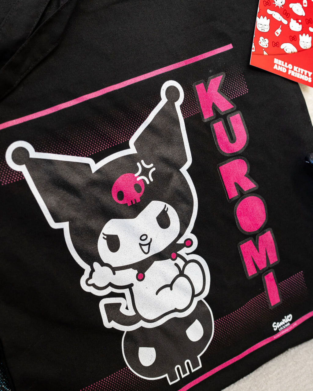 A black tote bag featuring Kuromi in her classic mischievous pose on a skull, with bold pink accents and the text “Kuromi” vertically on the side. The bag is stylish, edgy, and perfect for fans of the Sanrio character.