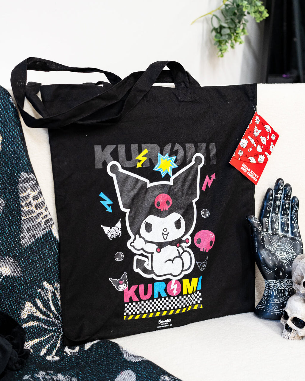 A black tote bag featuring Sanrio’s Kuromi in a colourful design with neon pink, blue, and yellow accents. The bag showcases Kuromi surrounded by lightning bolts, skulls, and fun punk-style details. Perfect for anime fans and alternative fashion lovers.