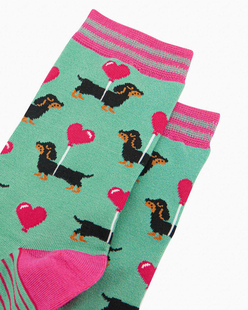 Close-up of the socks laid flat, showing the repeating pattern of dachshunds with love heart balloons on a mint green background.