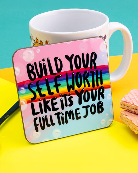 A colourful square coaster featuring a rainbow across a pink and blue pastel background with bubble details. Bold black text reads: “Build your self worth like it’s your full time job.” Designed by Katie Abey. The coaster is 9cm square with rounded corners and perfect for adding motivation to your workspace or coffee table.