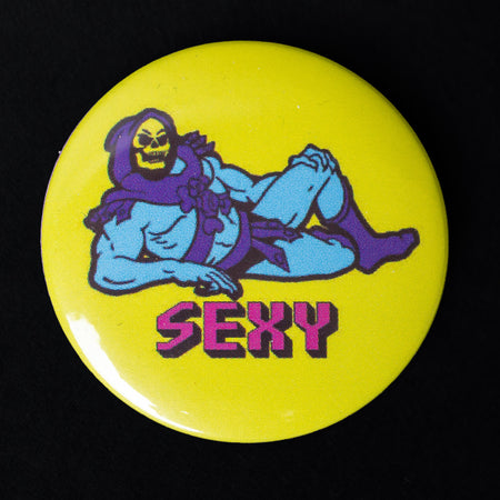 A 38mm button badge featuring Skeletor lounging provocatively on a bright yellow background with the word “SEXY” written in bold pink retro-style letters. This high-gloss pin is a cheeky nod to pop culture, perfect for personalising your accessories. Designed by Bite Your Granny.