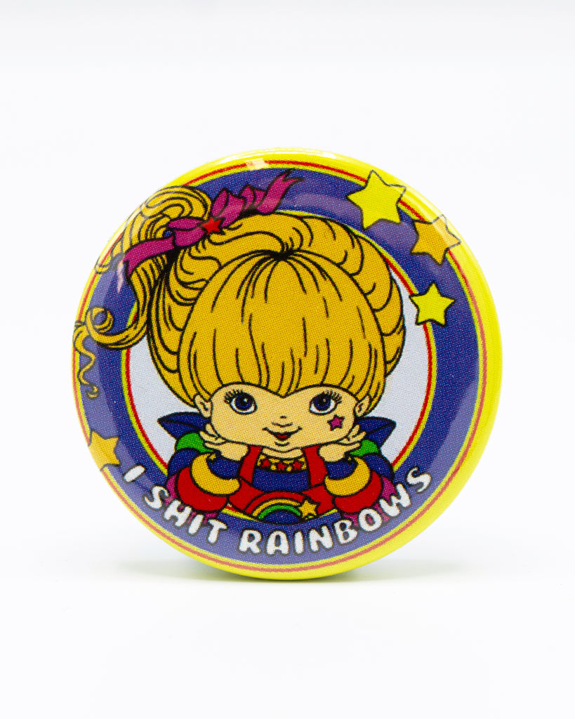 Blue and yellow button badge with a rainbow brite cartoon character smiling and white bubble writing that reads 'I shit rainbows'. An 80s nostalgic design by Bite Your Granny.