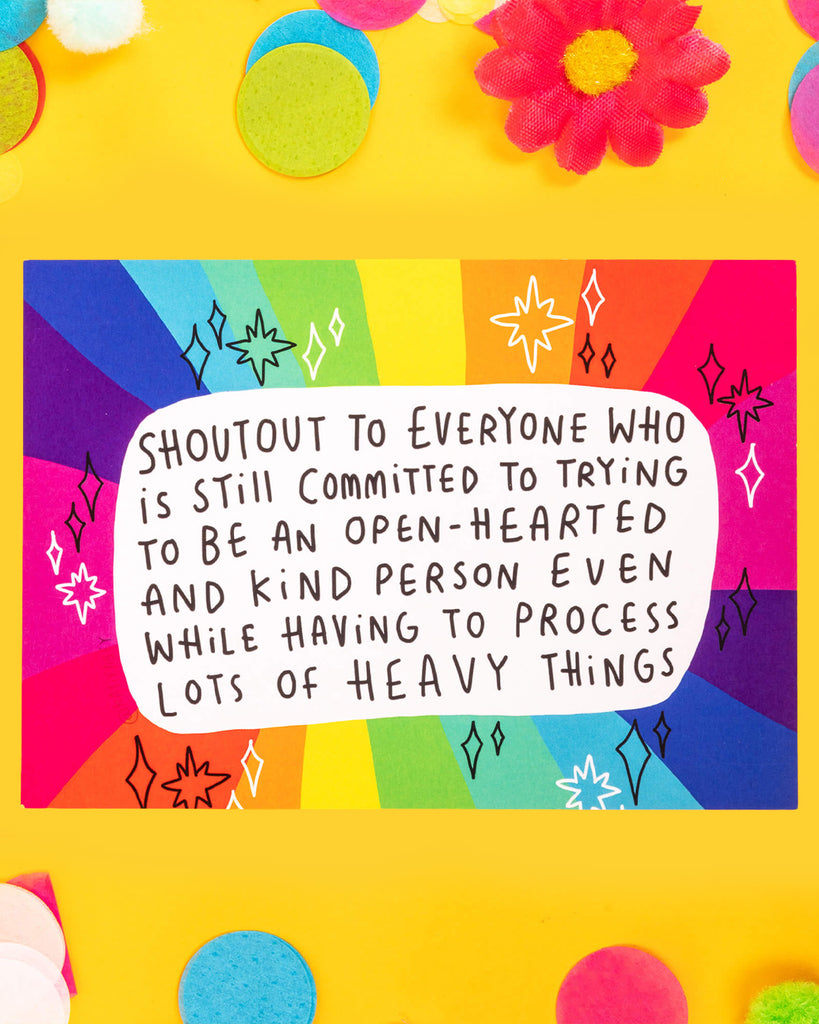 A colourful A6 postcard designed by Katie Abey with a rainbow background and black-and-white text that reads: “Shoutout to everyone who is still committed to trying to be an open-hearted and kind person even while having to process lots of heavy things.” The perfect uplifting message of emotional strength and kindness.