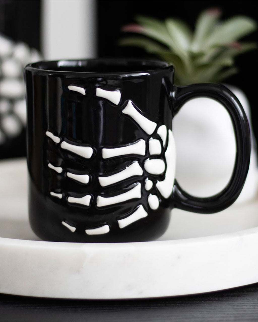 Close-up of a black ceramic mug featuring a raised white skeleton hand design, perfect for gothic or Halloween homeware lovers.