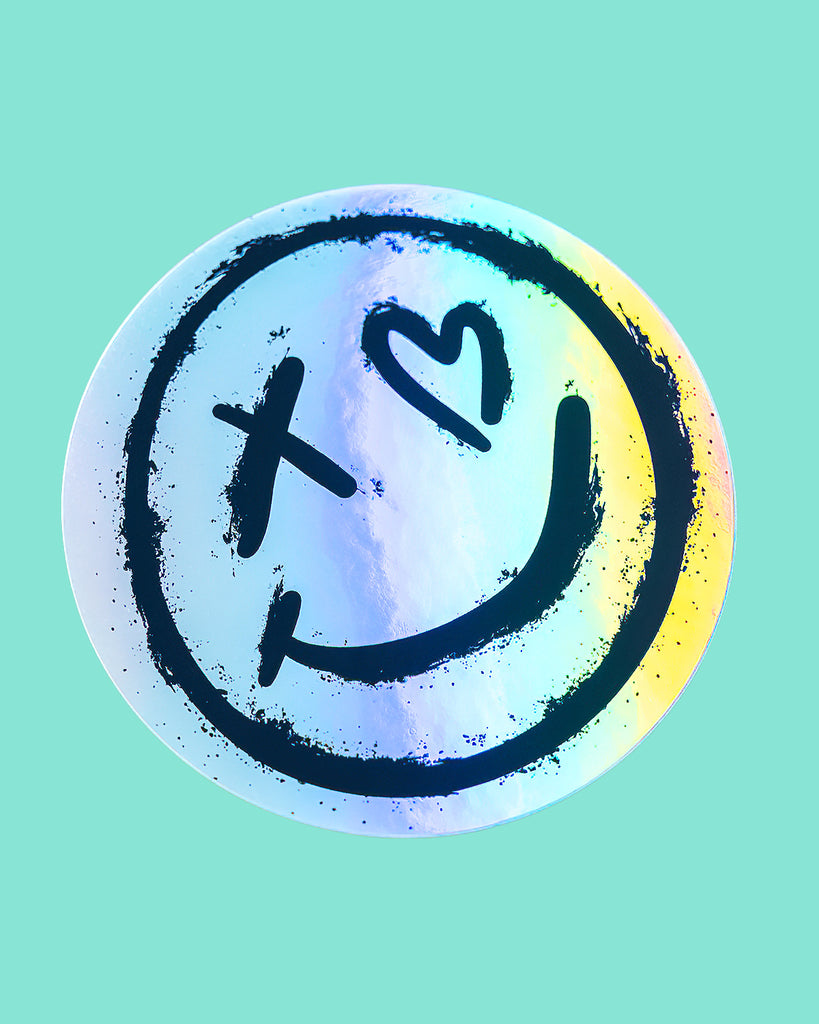 Holographic Rebel Romance logo sticker showcasing the iconic alternative-style smiley face design with a cross-shaped and heart-shaped eye. Ideal for adding a rebellious touch with shimmering colour to your favourite items.