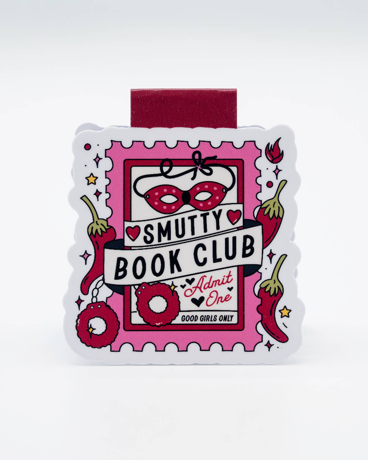 Front view of the Smutty Book Club Magnetic Bookmark from Rebel Romance, shaped like a raunchy pink ticket with illustrations of a mask, handcuffs, chillies, and hearts. Features the slogan “Good Girls Only” and “Admit One.” A fun and flirty gift for fans of steamy fiction and those who love to spice up their reading time with alternative accessories.