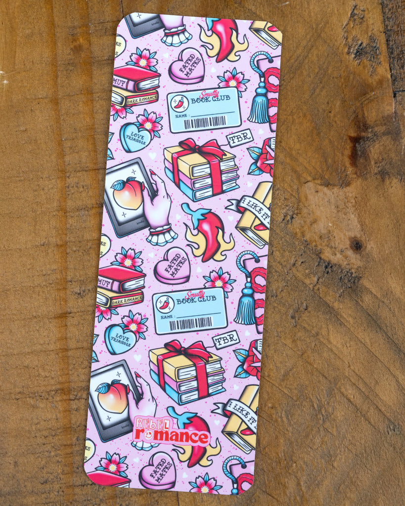 Smutty Book Club bookmark styled on a pink book. The pastel pink design is covered with fun illustrations like books, flowers, a phone with a peach emoji, flames, and a barcode name badge. A cute gift for spicy romance readers. Rebel Romance logo is at the bottom.
