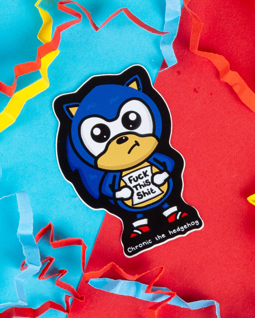 Glossy vinyl sticker of "Chronic the Hedgehog", a blue cartoon character inspired by Sonic, holding a sign that says “Fuck This Shit”. Designed by Innabox and sold by Rebel Romance, a UK brand known for alternative and retro aesthetics. Surrounded by colourful torn paper confetti on a bright red and turquoise background. Ideal for laptops, planners or water bottles.