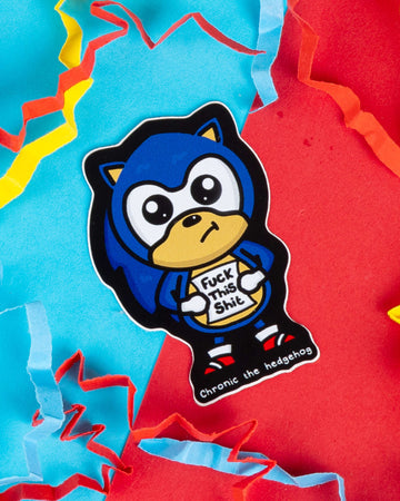 Glossy vinyl sticker of "Chronic the Hedgehog", a blue cartoon character inspired by Sonic, holding a sign that says “Fuck This Shit”. Designed by Innabox and sold by Rebel Romance, a UK brand known for alternative and retro aesthetics. Surrounded by colourful torn paper confetti on a bright red and turquoise background. Ideal for laptops, planners or water bottles.