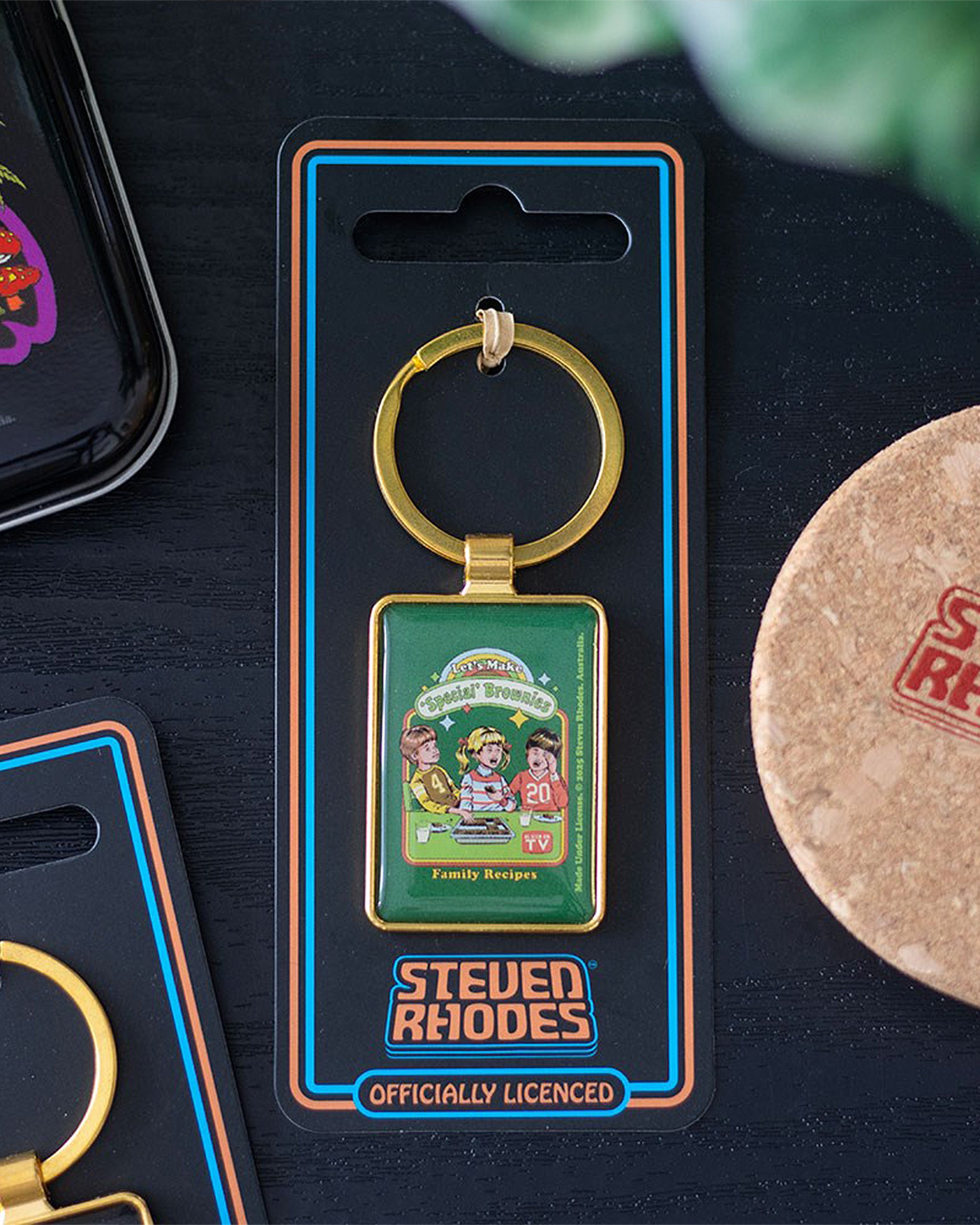 Lifestyle image of Rebel Romance Let's Make 'Special' Brownies keyring by Steven Rhodes. Quirky enamel keychain in retro packaging displayed on a dark surface. Fun alternative gift for millennials who love humour, nostalgia, and rebellious pop culture style.