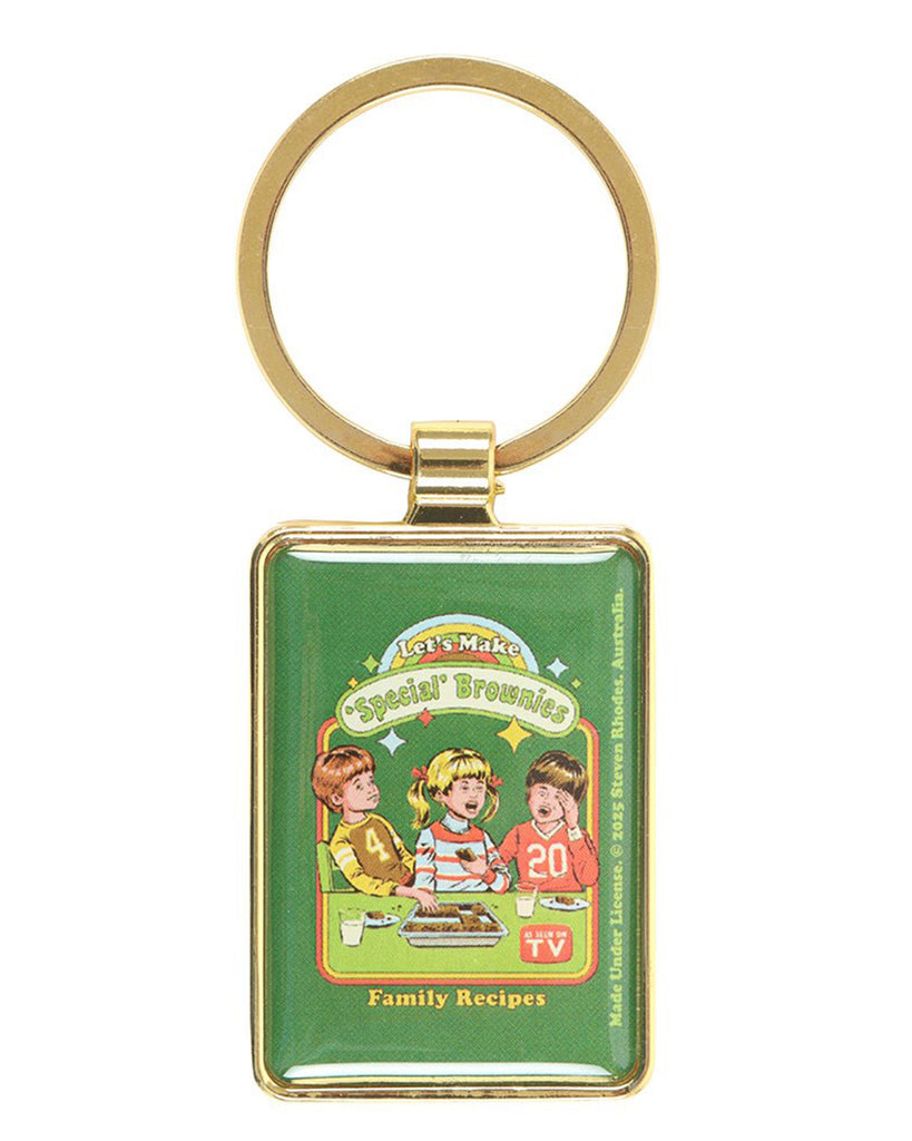 Rebel Romance Let's Make 'Special' Brownies enamel keyring by Steven Rhodes shown flat. Green retro design with vintage kids baking illustration, framed in a gold-tone keychain. Fun and edgy alternative gift idea with a cheeky twist on family recipes.