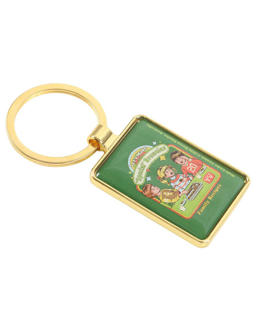 Side angle view of Rebel Romance Let's Make 'Special' Brownies keyring, designed by Steven Rhodes. Gold-tone enamel keyring with retro kids baking illustration. Alternative quirky gift, perfect for herbal enthusiasts, nostalgic humour fans, and collectors of Steven Rhodes licensed accessories.