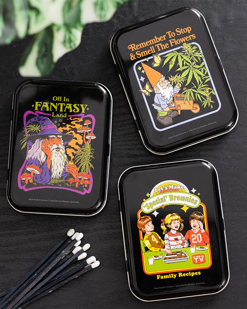 A set of retro stash tins from Rebel Romance, featuring Steven Rhodes designs with dark humour. The “Let’s Make Special Brownies” tin is shown alongside “Off in Fantasy Land” and “Remember to Stop & Smell the Flowers”. Perfect quirky homeware gift for millennials who love alternative style, humour, and unique storage solutions.