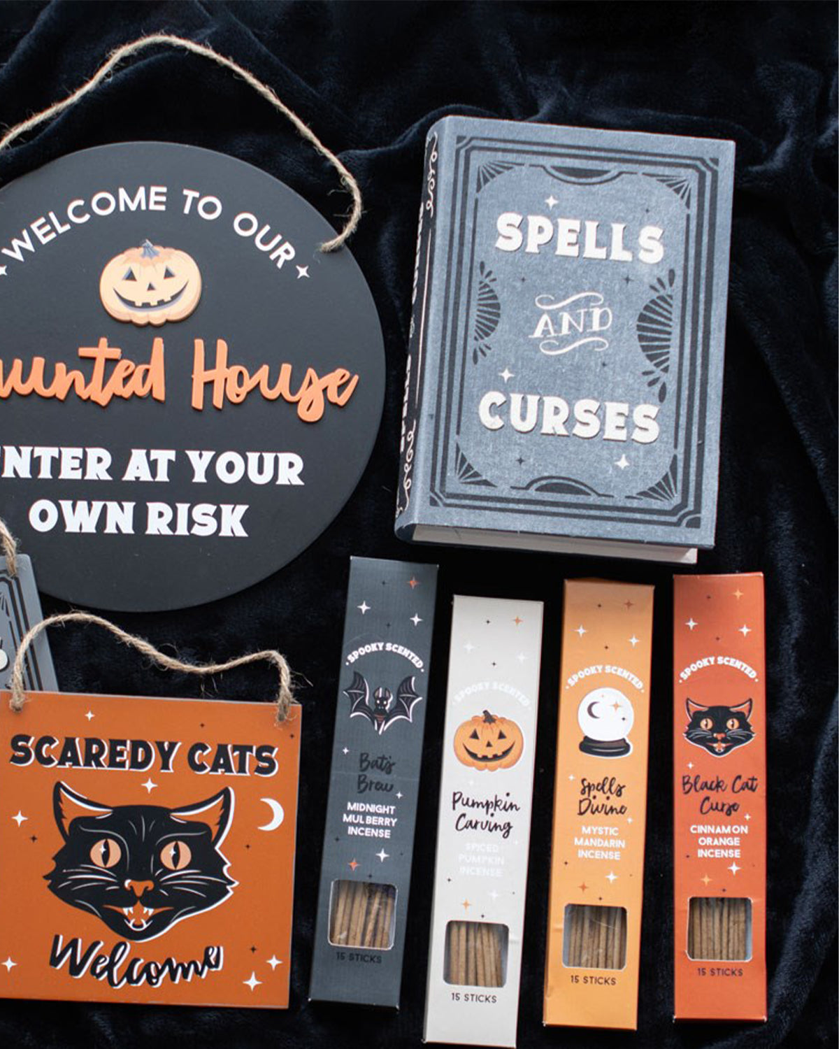 A Halloween-themed flat lay featuring the Spells and Curses Book Shaped Storage Box from goth shop Rebel Romance, surrounded by gothic decor. The black and grey book-shaped box is styled with incense, spooky signs, and a black velvet background, creating a witchy aesthetic.