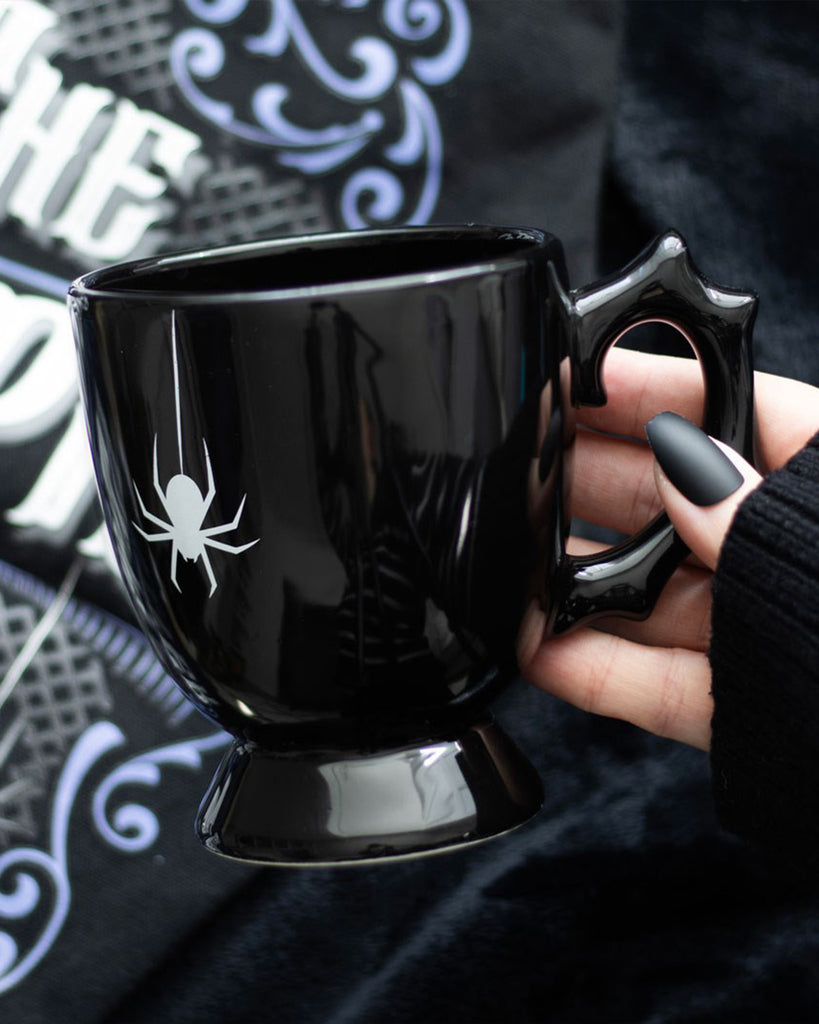 Close-up of a hand holding the Black Spider Teacup with a white spider print and sculpted thorn-like handle.