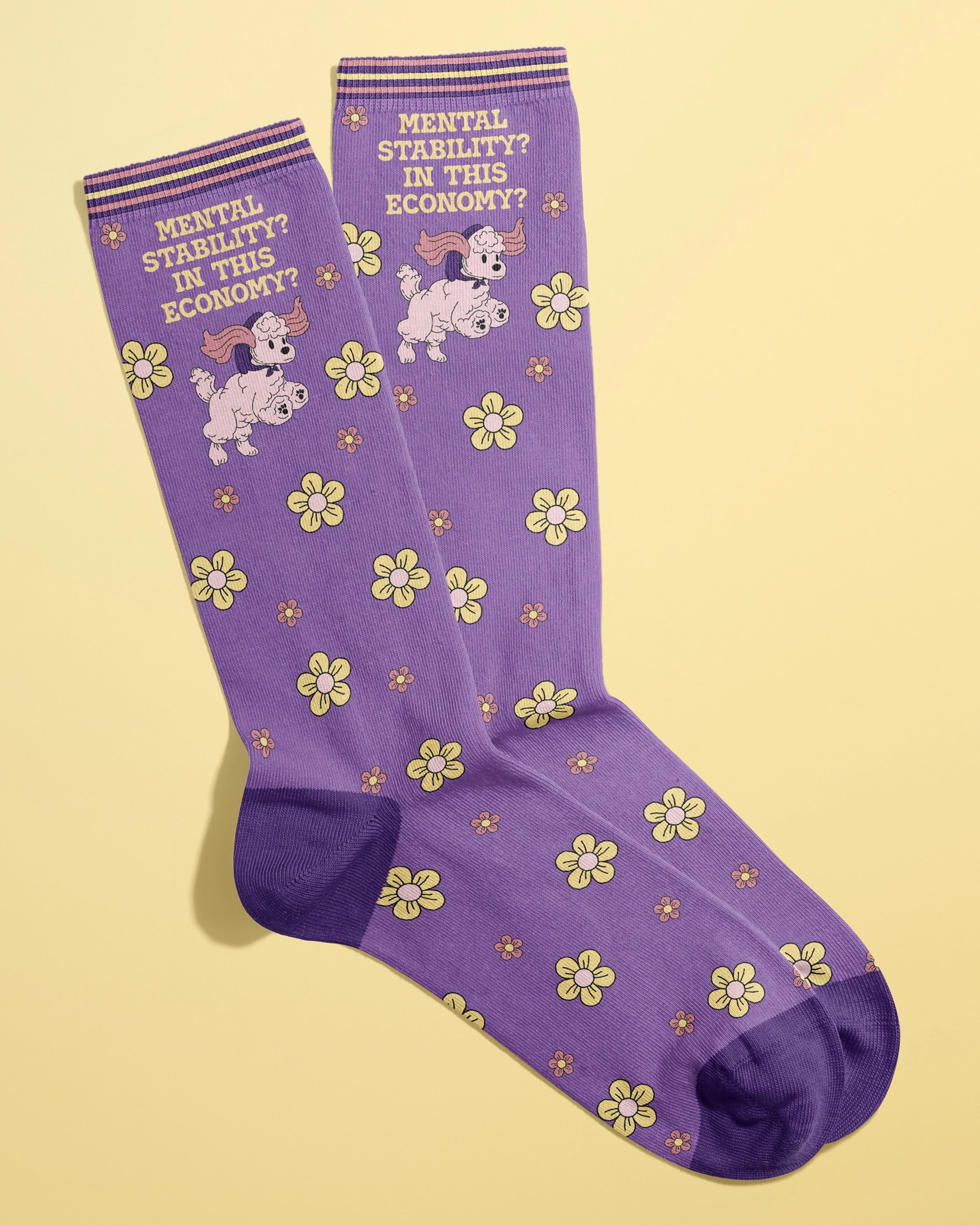 Pair of purple crew socks from Rebel Romance featuring a poodle illustration, yellow and pink flowers, and the phrase “Mental Stability? In This Economy?” across the top. Made by FUN CLUB and designed for alternative millennial fashion lovers.