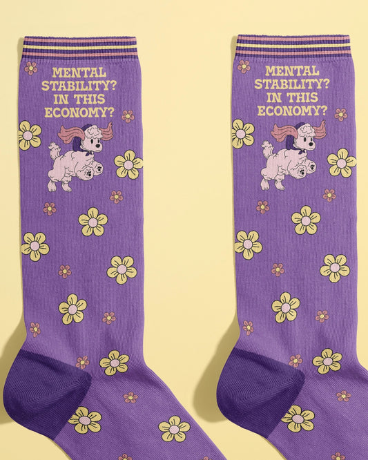 Close-up of purple Rebel Romance novelty socks with yellow and pink floral pattern and a sassy poodle design. The slogan “Mental Stability? In This Economy?” appears in bold text. Ethically made by FUN CLUB for a quirky millennial audience.